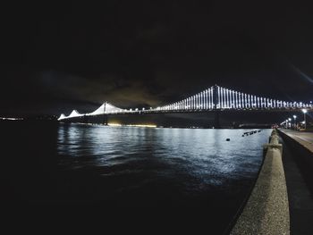 Illuminated bridge over sea against sky at night