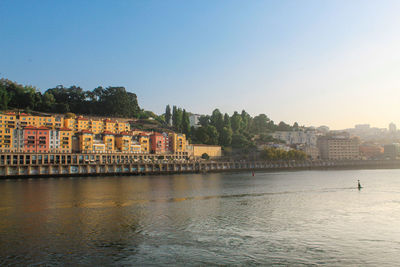 Buildings by river against clear sky