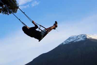 Low angle view of man hanging on mountain against sky