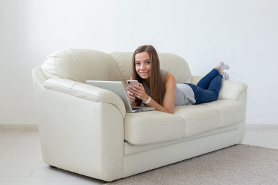 Young woman using phone while sitting on sofa at home