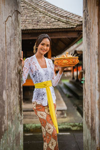 Portrait of young woman standing against tree trunk