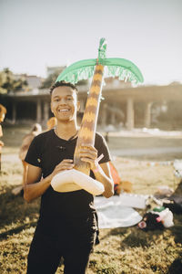 Portrait of smiling young man holding balloon while standing in lawn at music concert