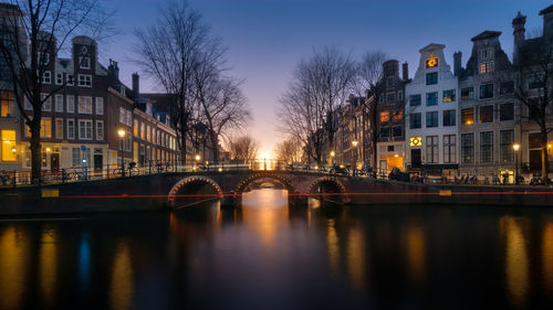 Illuminated bridge over river amidst buildings in city at night