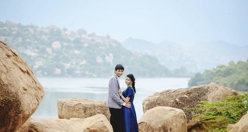 Smiling man and woman standing amidst rocks against river