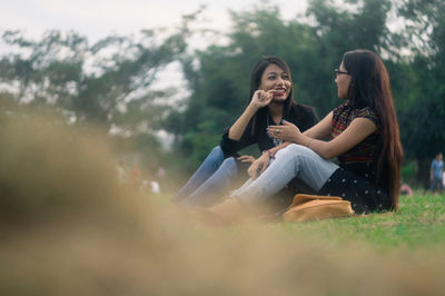 Smiling friends sitting on field against sky