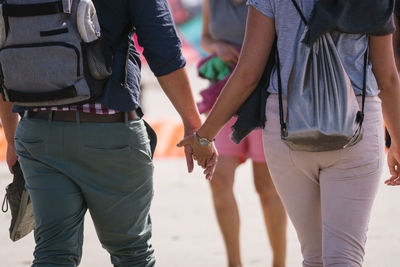 Rear view midsection of couple walking while holding hands on street