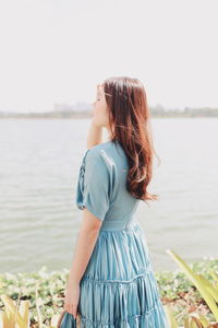 Side view of young woman standing at lakeshore against clear sky
