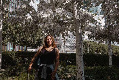 Portrait of smiling young woman standing against trees