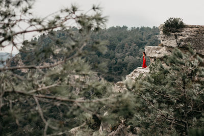 Woman with red dress  standing on rock against sky