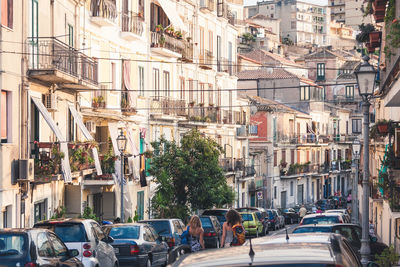 Rear view of women walking by cars on street in city