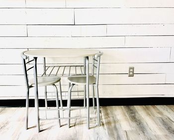 Empty chairs and table against white wall