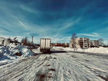 Snow covered land by buildings against sky