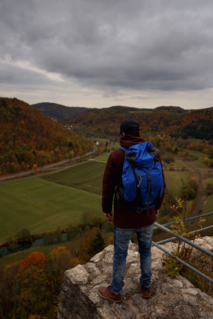 one person, sky, cloud - sky, scenics - nature, standing, rear view, mountain, full length, beauty in nature, real people, men, non-urban scene, leisure activity, backpack, nature, activity, casual clothing, environment, lifestyles, mountain range, outdoors, looking at view