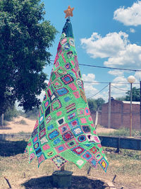 Multi colored decorations hanging on tree by field against sky