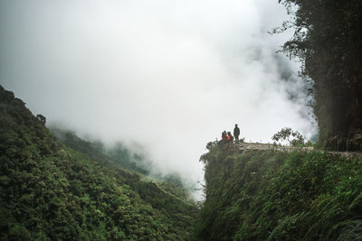 People on cliff against cloudy sky during winter