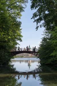 People on footbridge over lake against sky