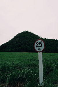 Road sign on field against sky