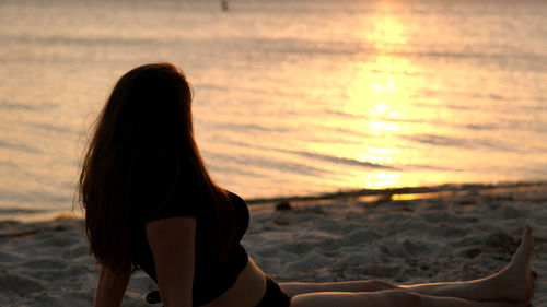 Rear view of woman sitting at beach during sunset