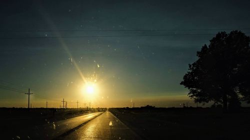 Road amidst silhouette trees against sky during sunset