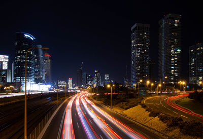 Light trails on road amidst buildings in city at night