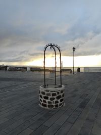 Empty footpath by street against sky during sunset