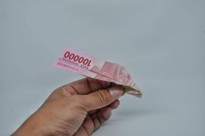 Close-up of hand holding paper against white background