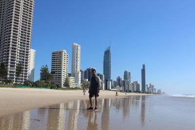 Man on beach by modern buildings against clear sky