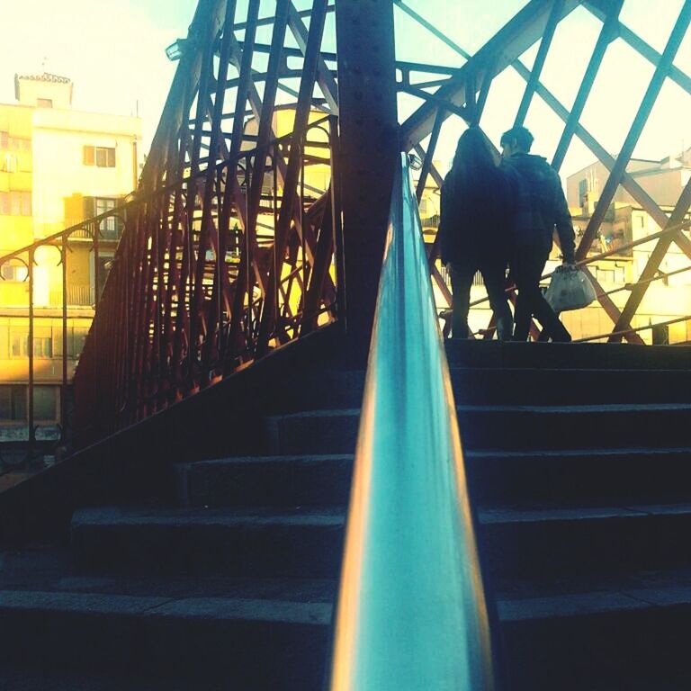 men, railing, lifestyles, transportation, rear view, low angle view, built structure, silhouette, architecture, leisure activity, connection, person, escalator, railroad track, bridge - man made structure, sky, standing, rail transportation