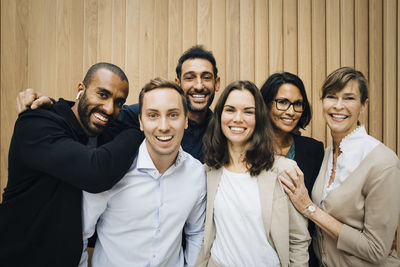 Portrait of happy male and female entrepreneurs standing against wooden wall