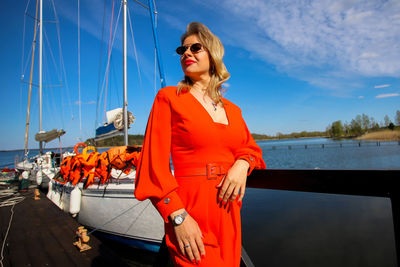 Young woman wearing sunglasses standing by boat against sky