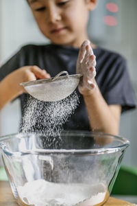 The child cooks in the kitchen. sifts the flour.