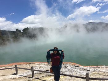 Woman covering eyes with scarf on mountain by lake against sky