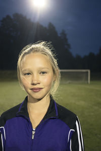 Portrait of confident girl standing on soccer field at night