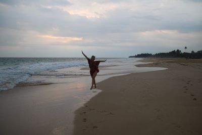 Woman dancing at beach against sky during sunset
