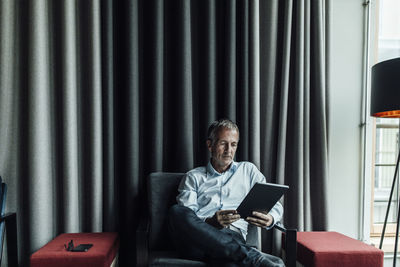 Serious businessman using digital tablet against gray curtain in office cafeteria