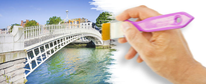 Close-up of hand holding bridge over river against sky