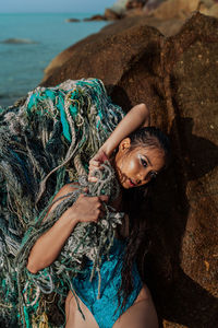 A young girl stands by a rock in a blue bodysuit and holds the ropes