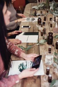 High angle view of female colleagues are sitting at table with various perfume bottles and brochures in workshop