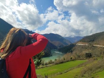 Rear view of woman photographing valley against cloudy sky