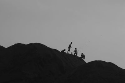 Silhouette people on rock against clear sky