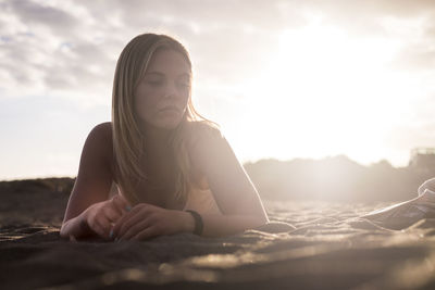 Young woman relaxing on sand at beach against sky