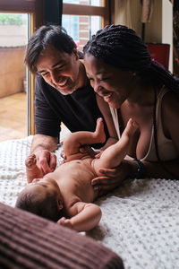 Caring african american mom changing diapers on infant lying on blanket with hispanic dad