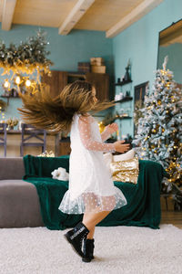 Stylish girl in a white dress whirls on the background of a christmas tree in the living room