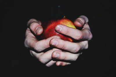 Close-up of hand holding strawberry over black background