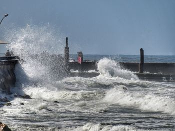 Waves splashing on shore against clear sky