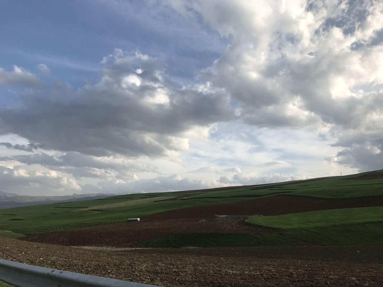 sky, cloud, environment, horizon, landscape, field, nature, plain, hill, land, scenics - nature, road, beauty in nature, grass, rural area, grassland, no people, plant, tranquility, rural scene, transportation, prairie, tranquil scene, day, green, non-urban scene, outdoors, cloudscape, travel, agriculture, horizon over land, sunlight