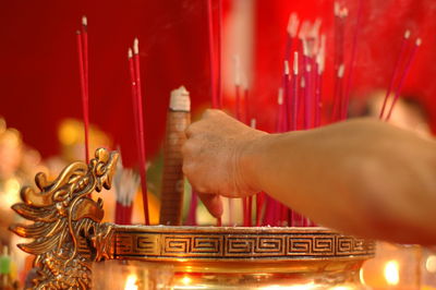 Close-up of hand holding incense sticks over container at temple