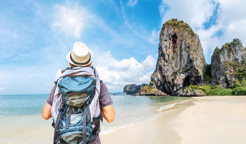 Rear view of person on rock at beach against sky