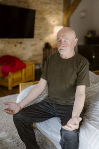 Senior man practicing yoga while sitting on bed at home