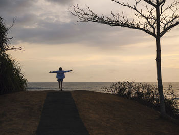 Woman with raised arms standing at the sea at sunset